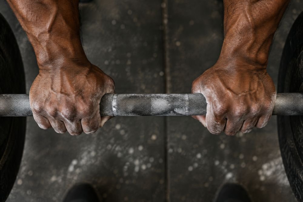 Chalked hands gripping a loaded barbell, knuckles and forearm tendons standing out